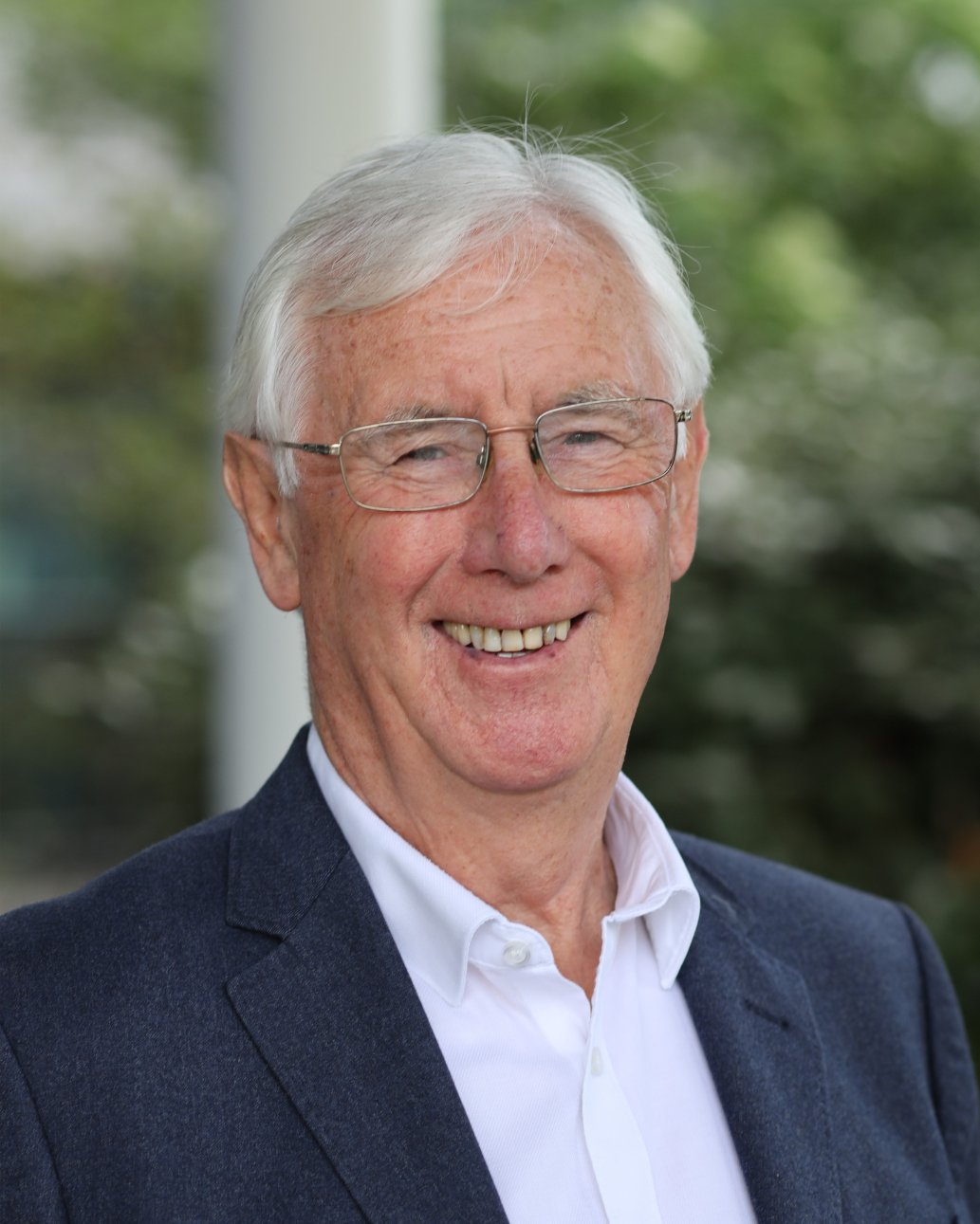 Les Walton CBE smiling in a navy jacket and white shirt
